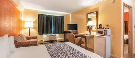 Habitación de hotel con una cama grande, un escritorio con computadora, televisión, microondas y refrigerador pequeño.