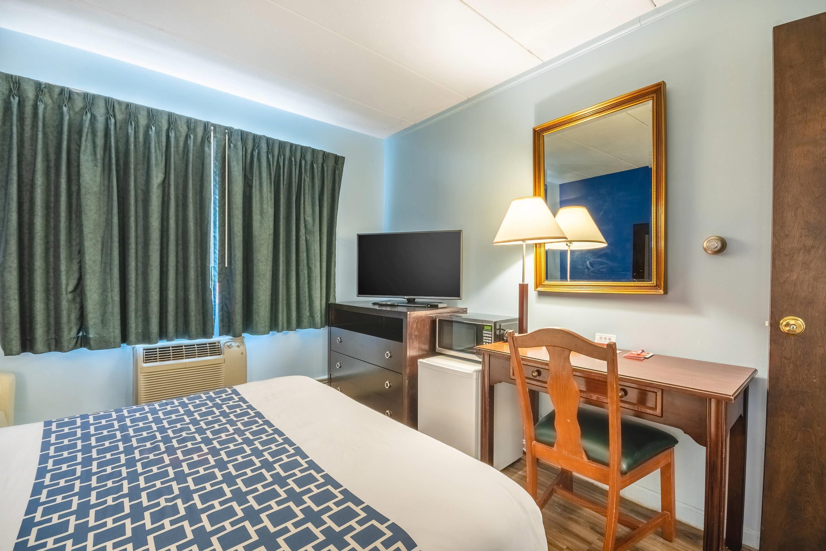 Ein Hotelzimmer mit Bett, Schreibtisch, Fernseher, Lampe und Spiegel.