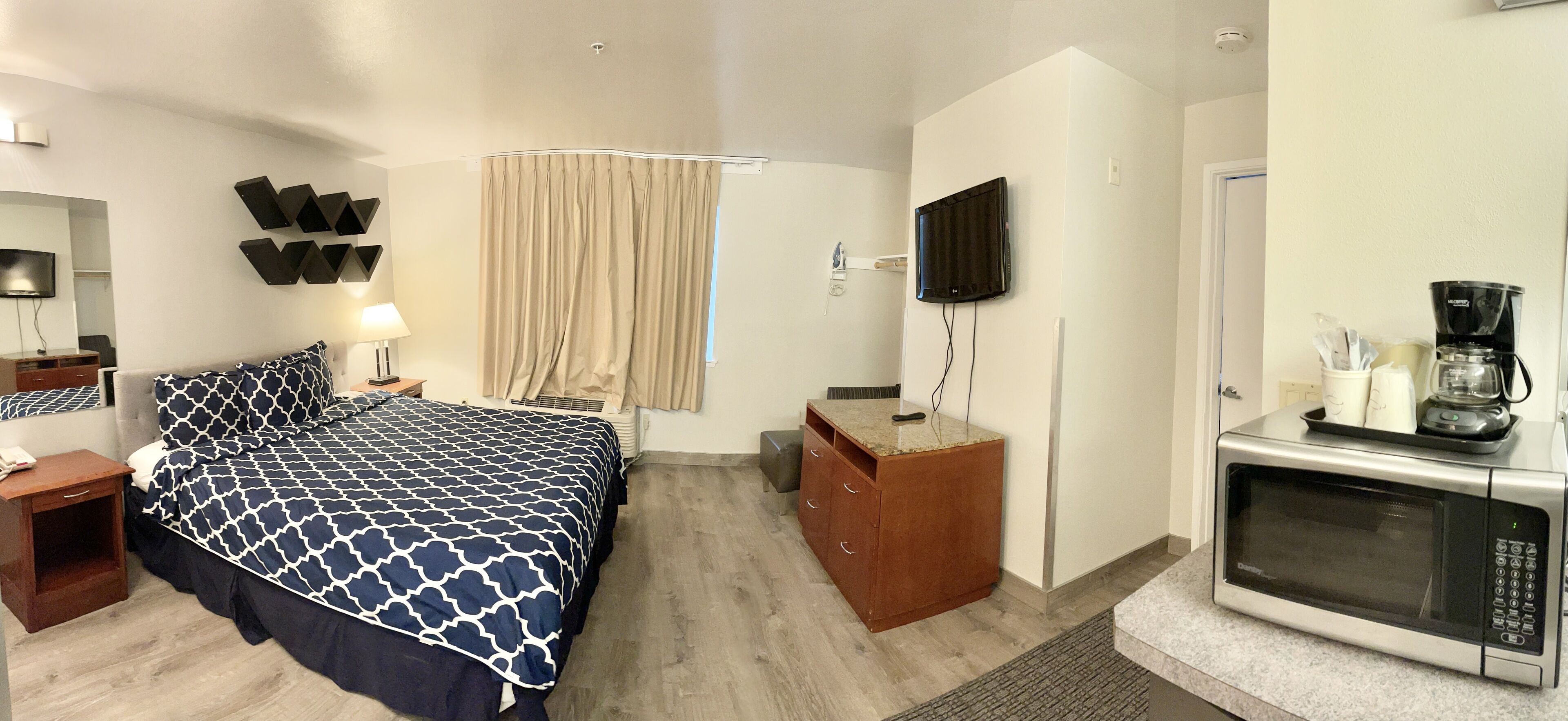 Habitación de hotel con cama, televisor, escritorio con microondas y ventana con cortinas.