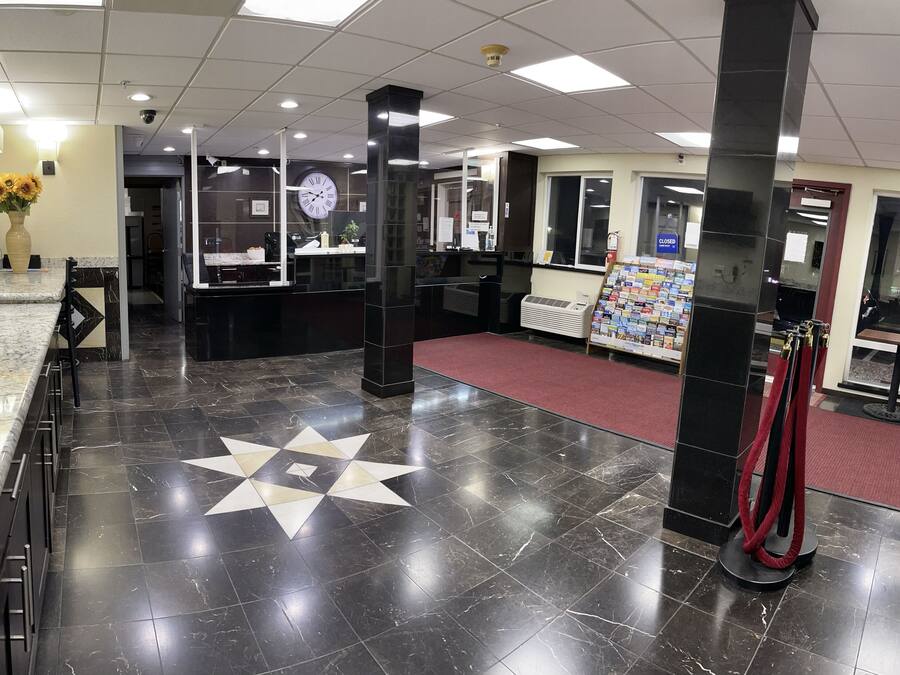 A lobby with a marble reception desk, a clock, a red carpet, and a display of magazines.