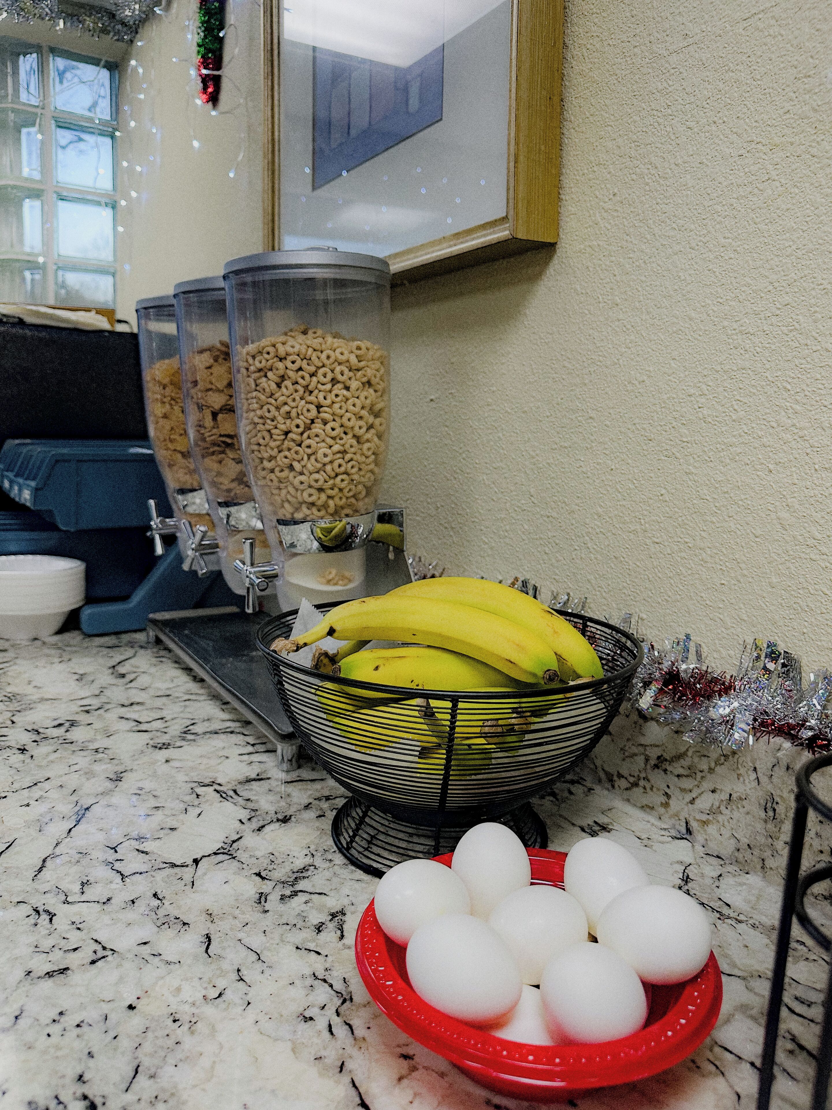 A kitchen counter with a blender, a bowl of bananas, and a red plate with eggs.