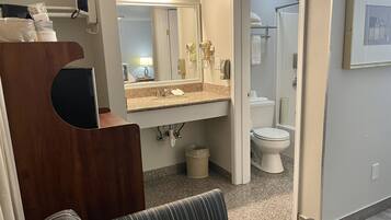 A bathroom with a sink, mirror, and toilet. There is a chair and a small table in the foreground.