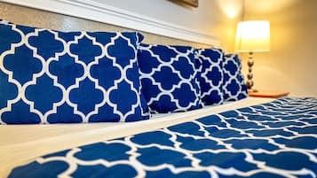 Un letto con lenzuola a motivi blu e bianchi, una lampada da comodino e un quadro appeso al muro.