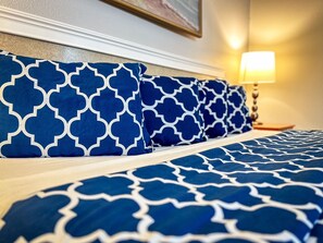 A bed with blue and white patterned bedding, a bedside lamp, and a framed picture on the wall.