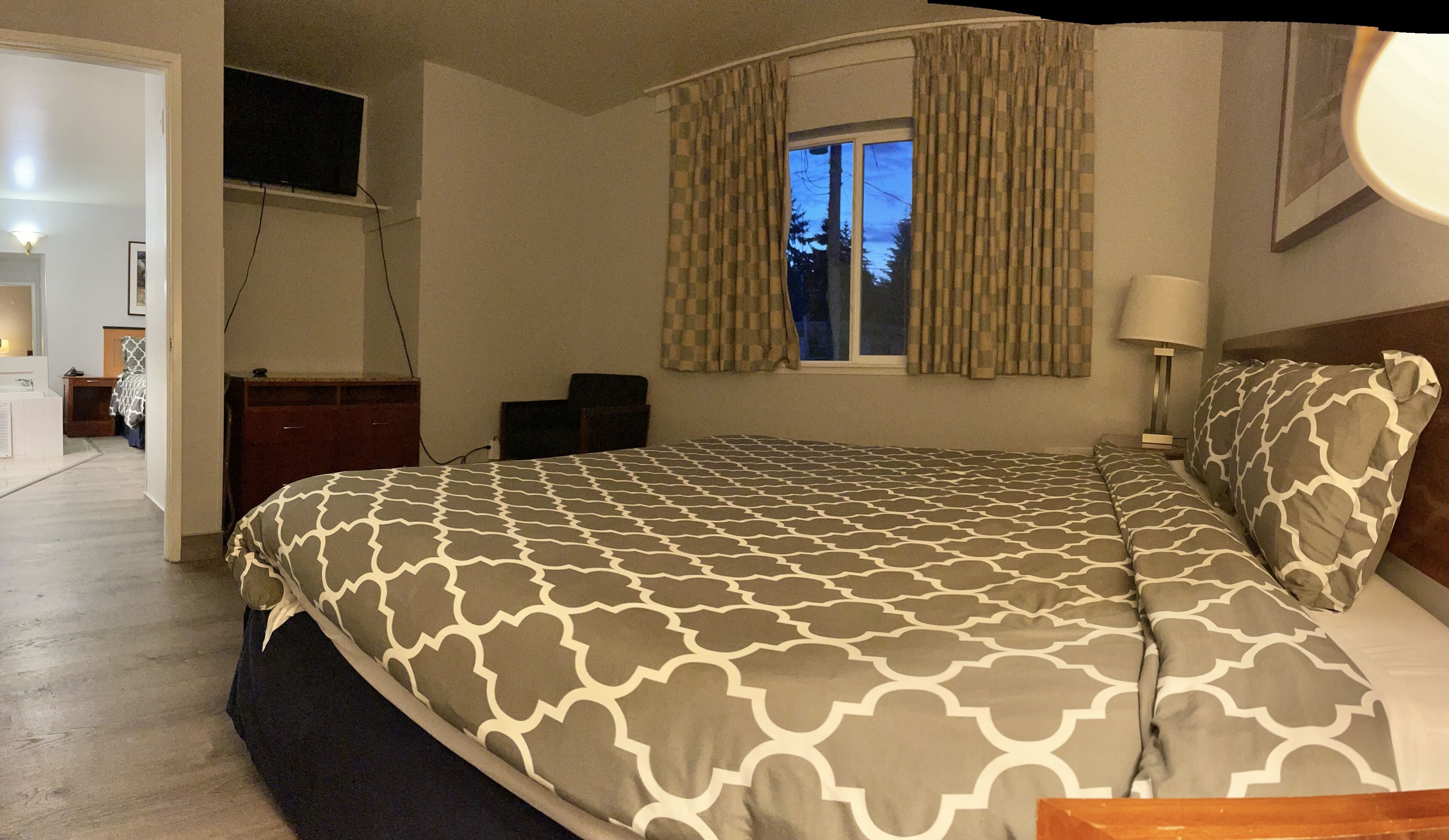 A bedroom with a bed, a desk, a chair, a window with curtains, and a TV mounted on the wall.