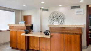 Un mostrador de recepción con acabado de madera, una estación de registro digital y un elemento decorativo en la pared.