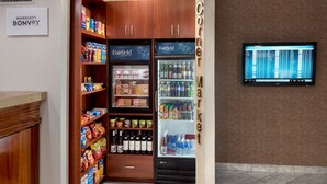 Un kiosco de esquina con un expositor refrigerado y estantes llenos de bocadillos y bebidas.
