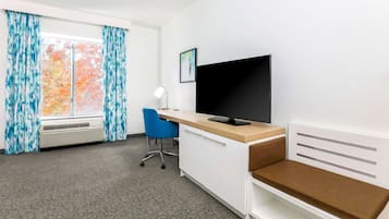 Habitación de hotel con escritorio, silla, televisor, ventana con cortinas y radiador.