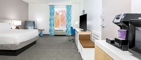 A hotel room with a bed, desk, TV, coffee machine, and a window with curtains.