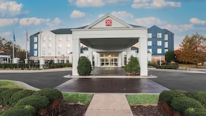 A hotel entrance with a covered walkway, a flag, and a clear sky. - Hilton Garden Inn Tulsa South (Tulsa)