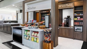 A coffee shop named "The Shop" with a refrigerated display, snack bags, and a coffee machine. - Hilton Garden Inn Tulsa South (Tulsa)