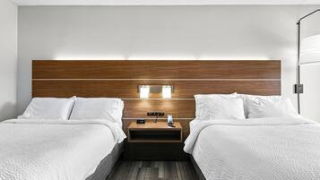 Una habitación de hotel con diseño moderno, que presenta dos camas con ropa blanca, un cabecero de madera, una mesita de noche con un reloj y una lámpara de pared.