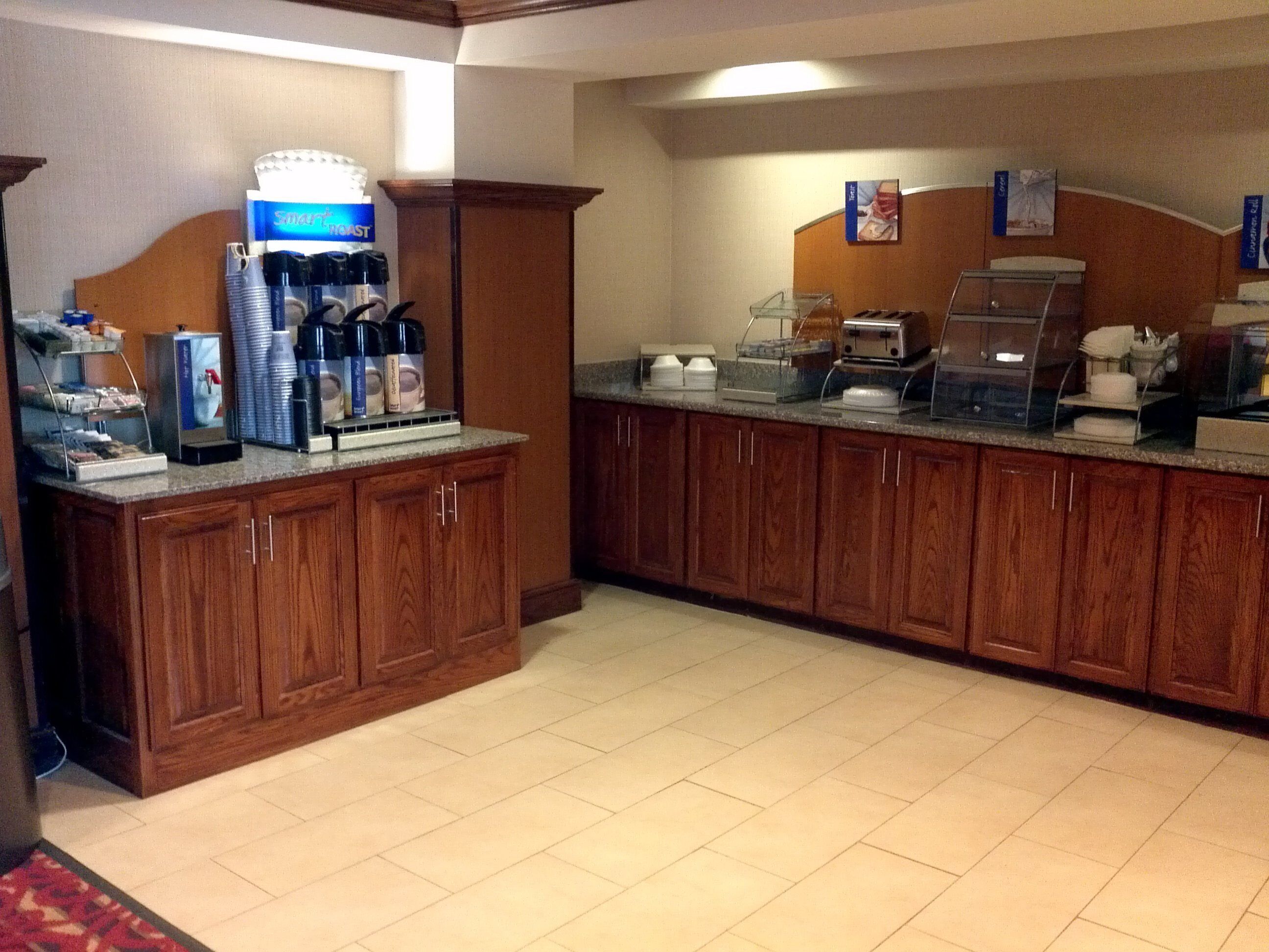A hotel breakfast area with wooden cabinets, a coffee station, and a buffet setup.