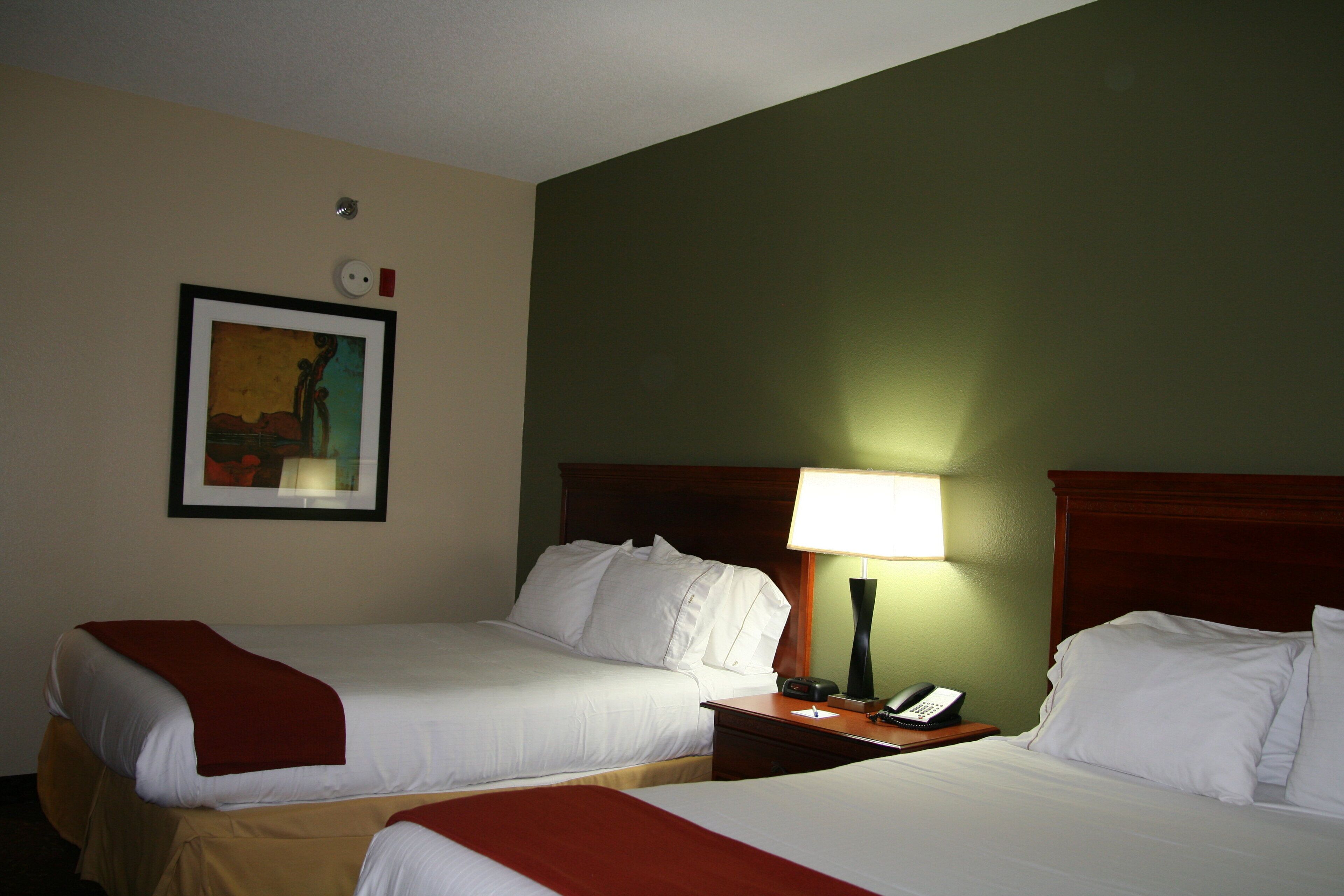 A hotel room with two beds, a nightstand with a lamp, a framed picture on the wall, and a telephone.