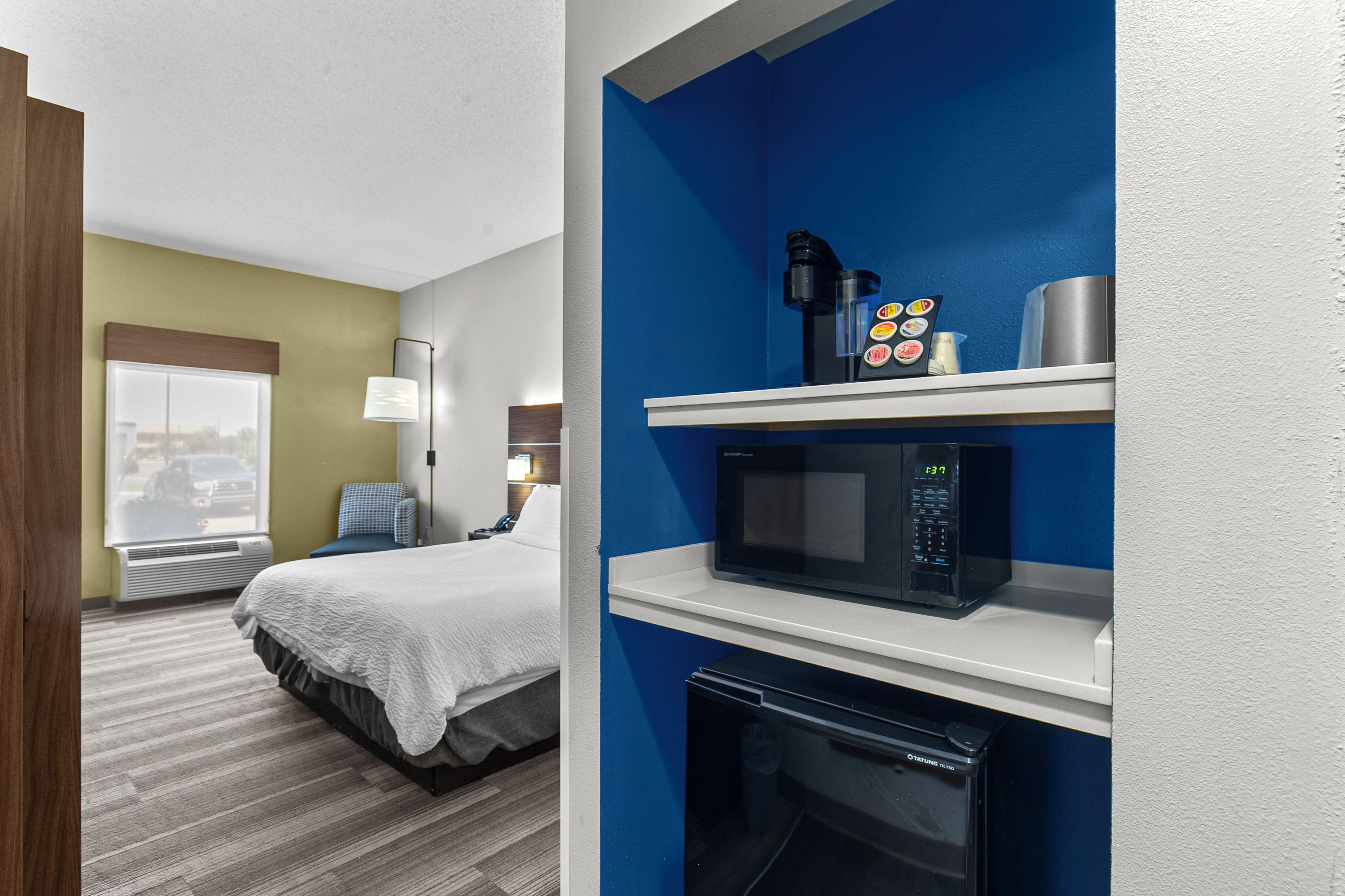Una habitación de hotel con una cama, un escritorio con lámpara, un microondas y una cafetera.