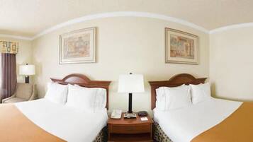 A hotel room with two beds, a nightstand, a lamp, and two framed pictures on the wall.