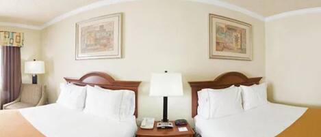A hotel room with two beds, a nightstand, a lamp, and two framed pictures on the wall.
