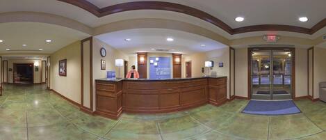A hotel reception area with a wooden reception desk, a clock, and a Holiday Inn Express sign.