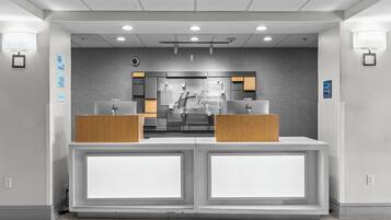 A hotel reception desk with a modern design, featuring a check-in counter, a digital display, and a wall-mounted sign indicating hotel services.