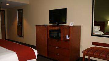 A hotel room with a bed, a wooden dresser with a television and microwave, a chair, and a mirror reflecting a bed and a nightstand.