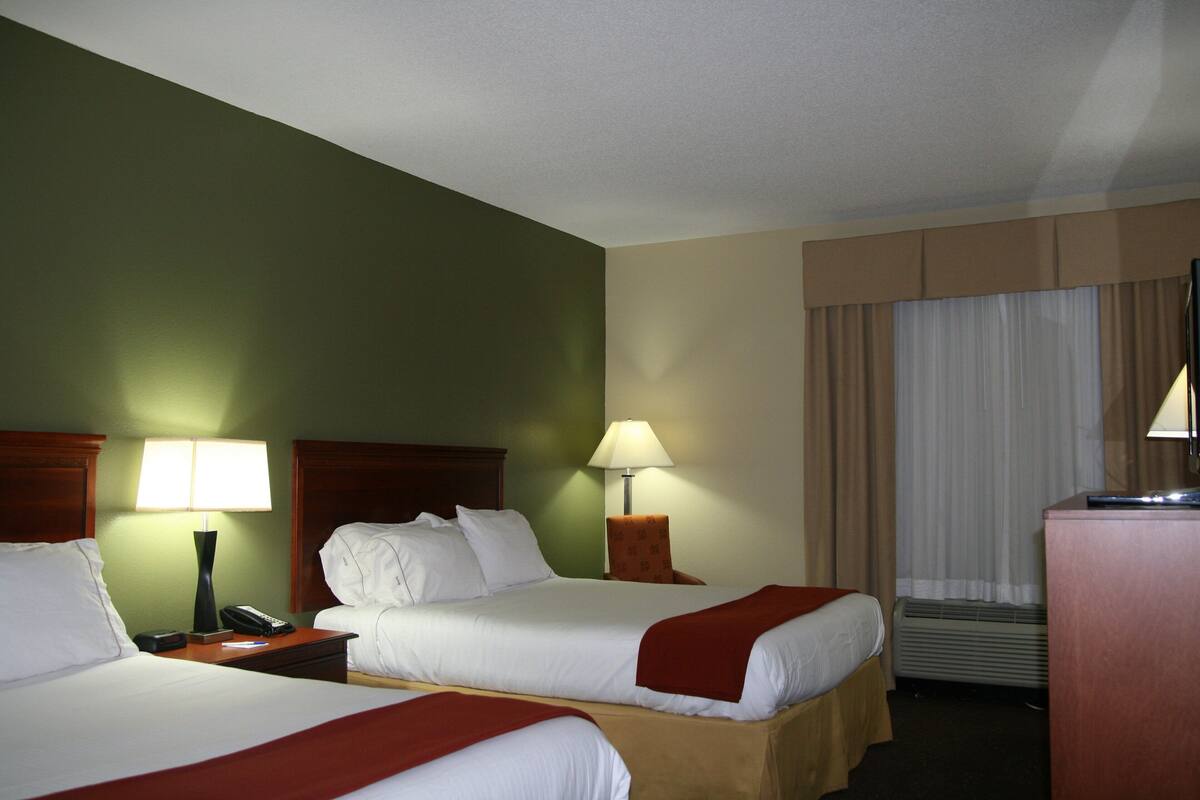 A hotel room with two beds, a desk, a chair, a lamp, and a television.