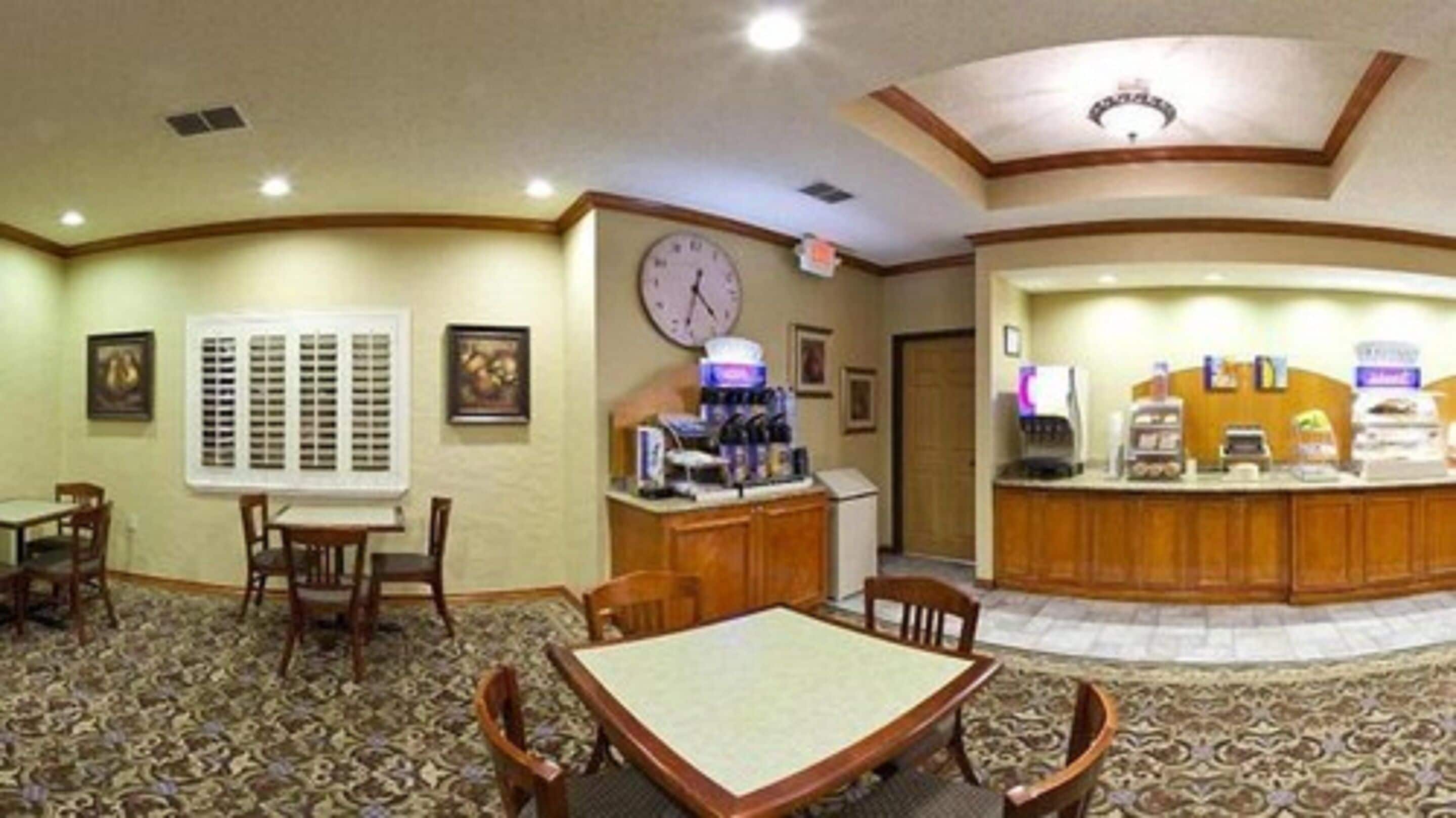 A hotel lobby with a reception desk, a clock, and a seating area with tables and chairs.