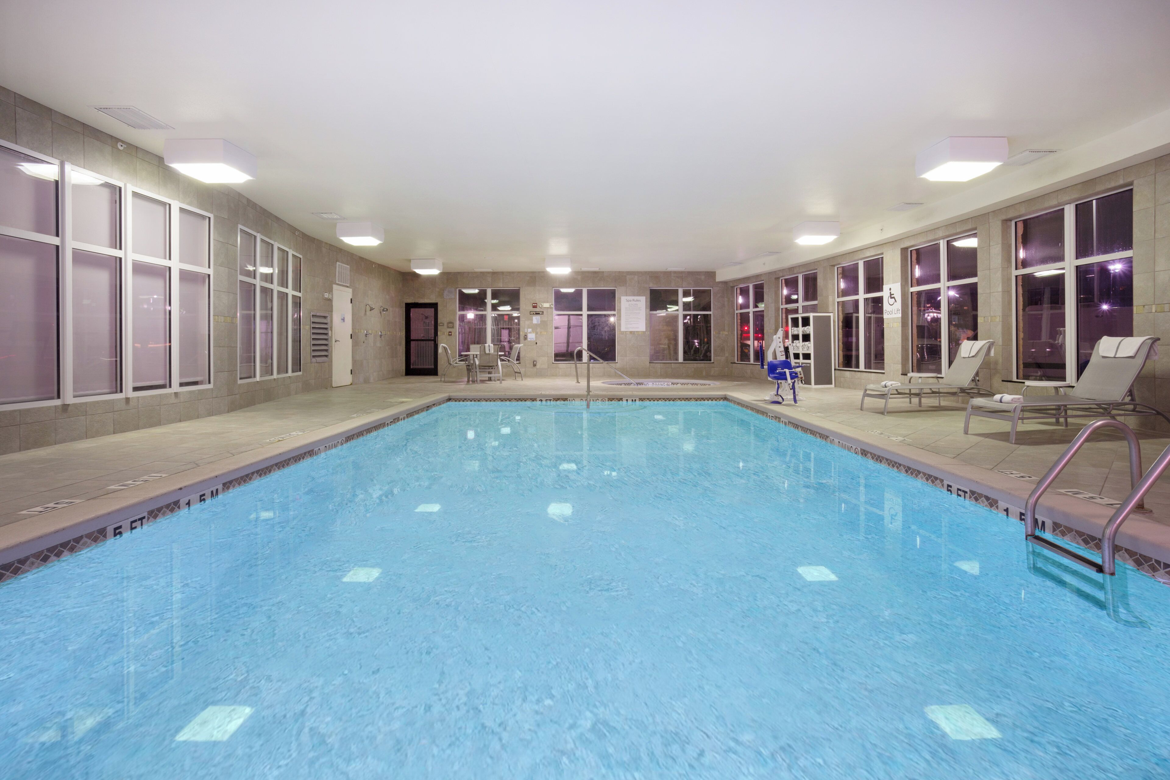 Une grande piscine intérieure à l’eau claire, entourée de murs dotés de grandes fenêtres et de portes, et dont le sol est carrelé.