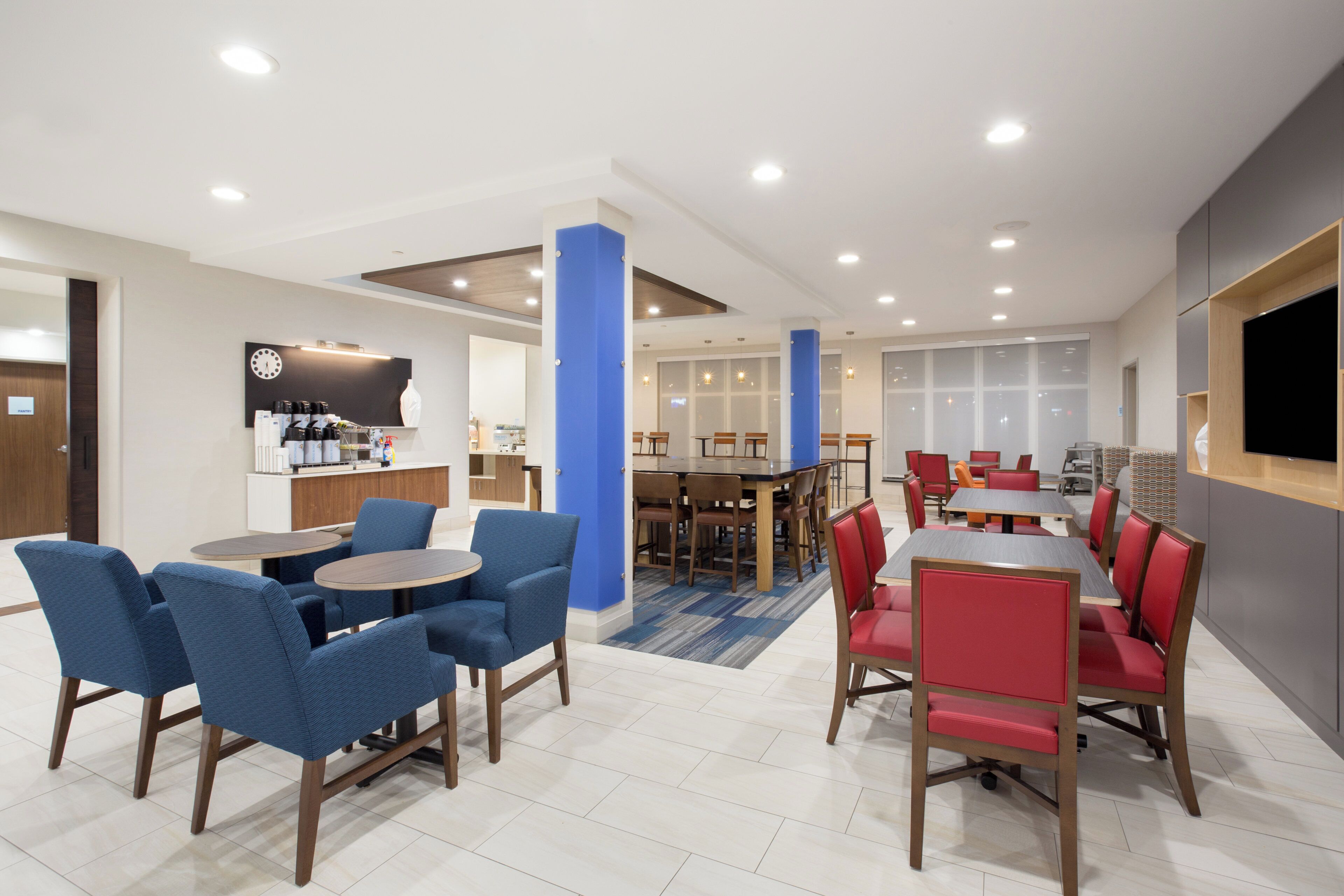 Un comedor moderno con sillas azules y rojas, una mesa central y una cocina al fondo.