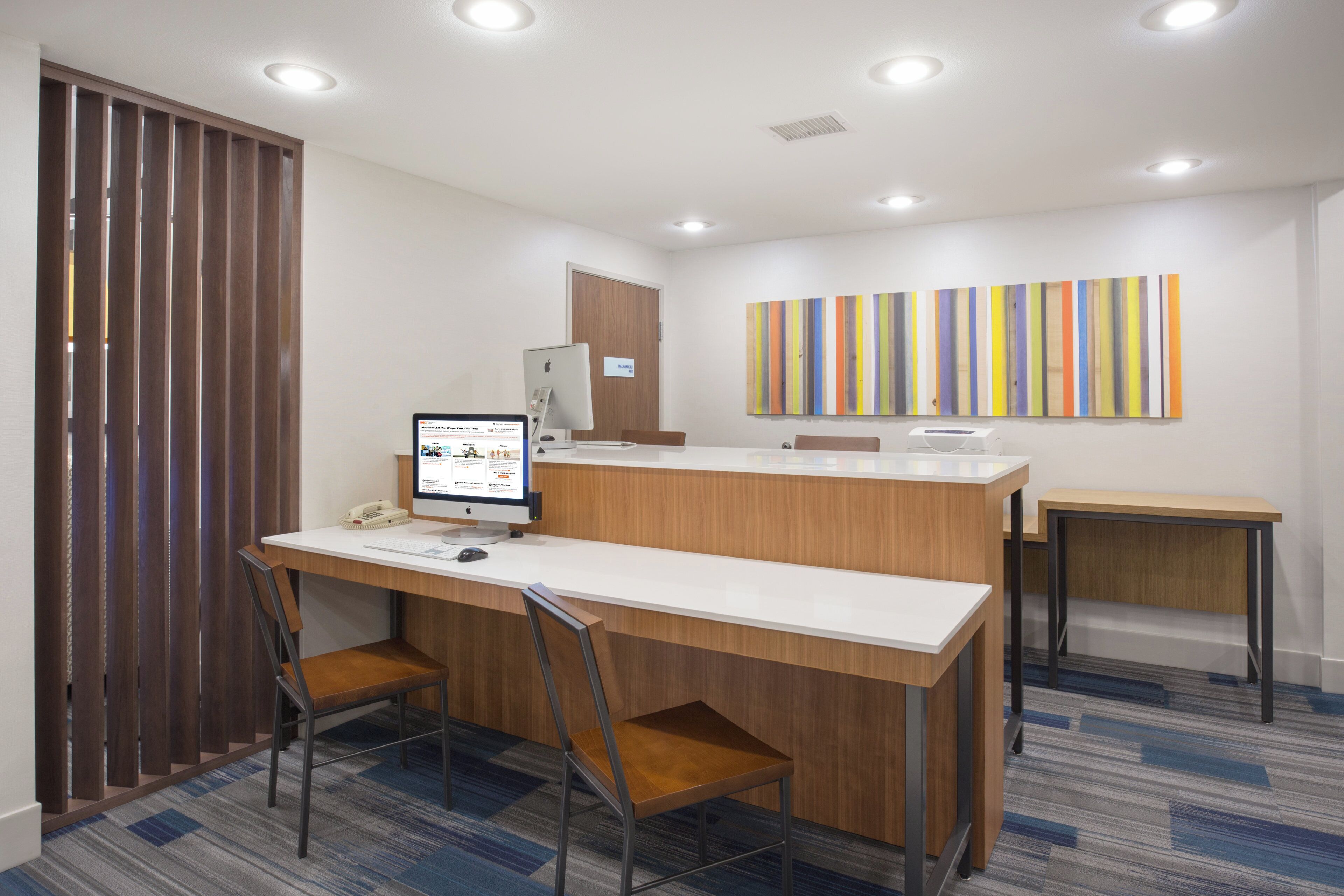 A modern office space with a desk, chairs, a computer, and a wall-mounted artwork.