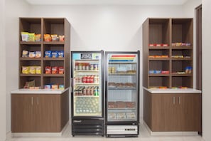 A vending machine with snacks and drinks, surrounded by wooden cabinets with various packaged goods. - Holiday Inn Express & Suites Amarillo by IHG (Amarillo)
