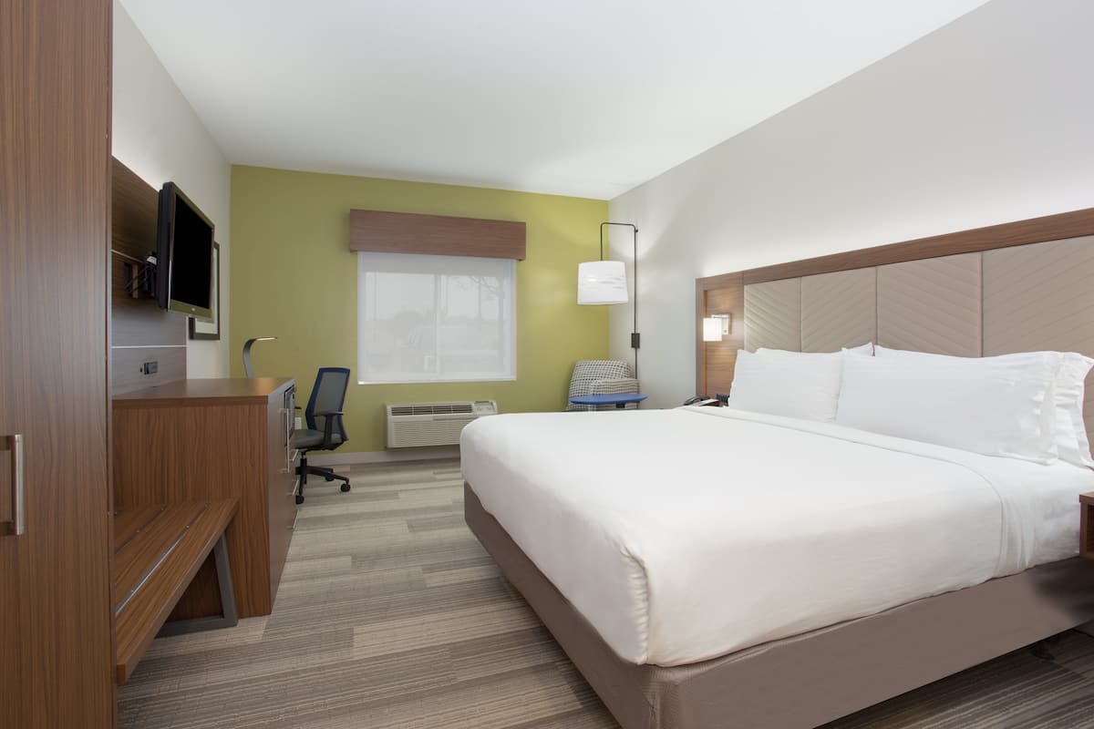 A hotel room with a bed, desk, chair, television, and a window with blinds.