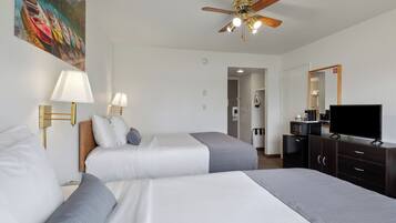 Habitación de hotel con dos camas, ventilador de techo, televisor y un cuadro en la pared.
