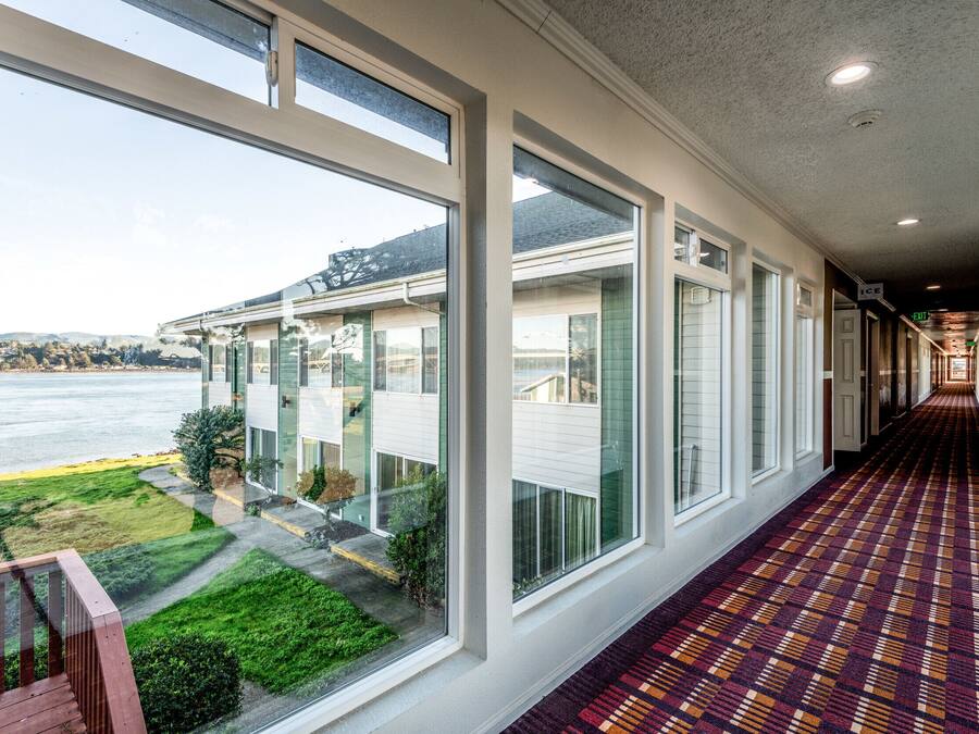 A hotel corridor with large windows, a patterned carpet, and a view of a body of water and greenery.