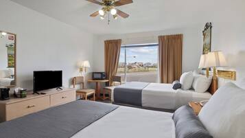 A hotel room with two beds, a television, a desk, a chair, a ceiling fan, and a window with curtains.