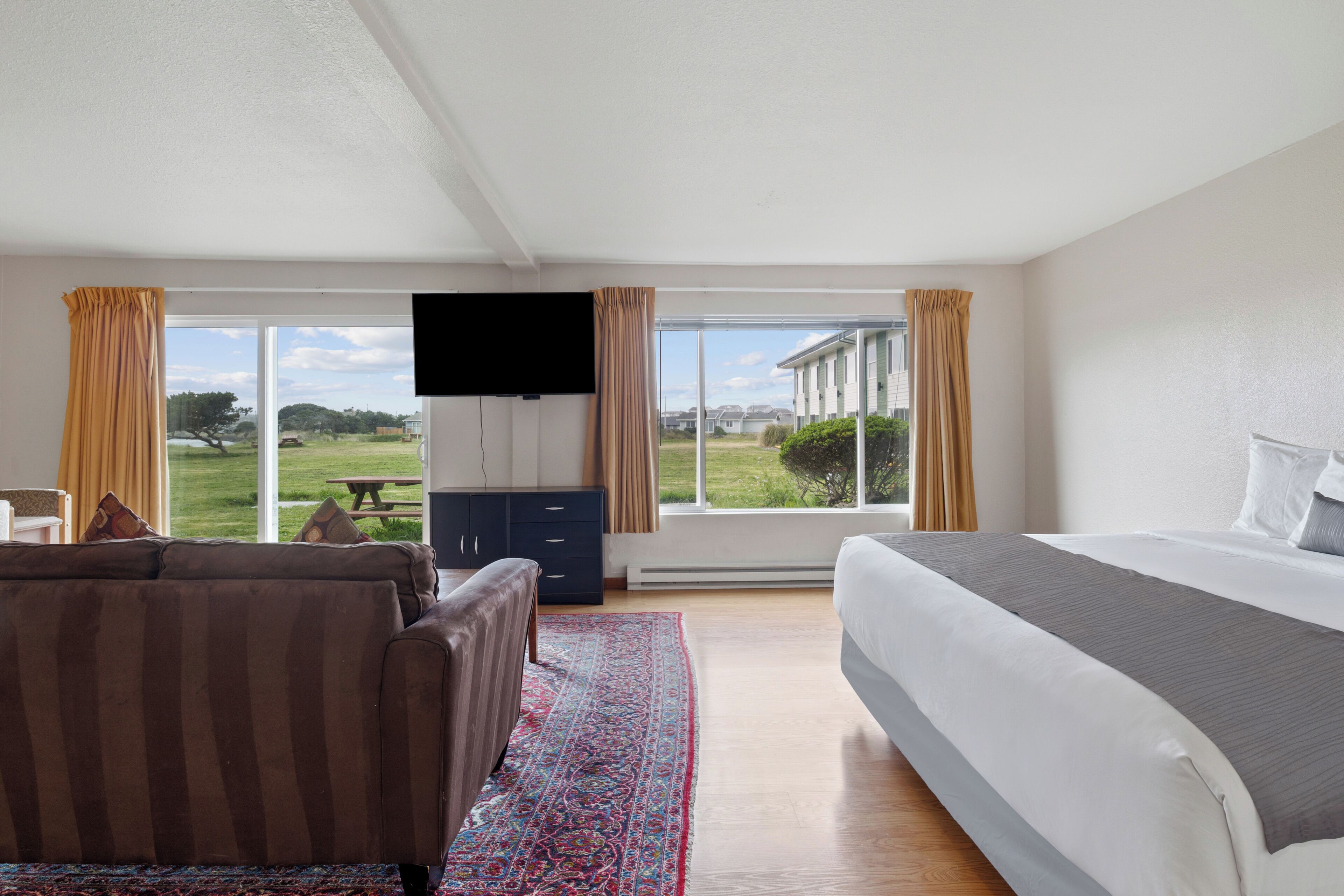 Une chambre avec un grand lit, un canapé, une télévision et une vue sur un paysage verdoyant grâce à de grandes fenêtres.
