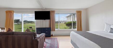 Un dormitorio con una cama grande, un sofá, un televisor y vistas a un paisaje verde a través de amplios ventanales.