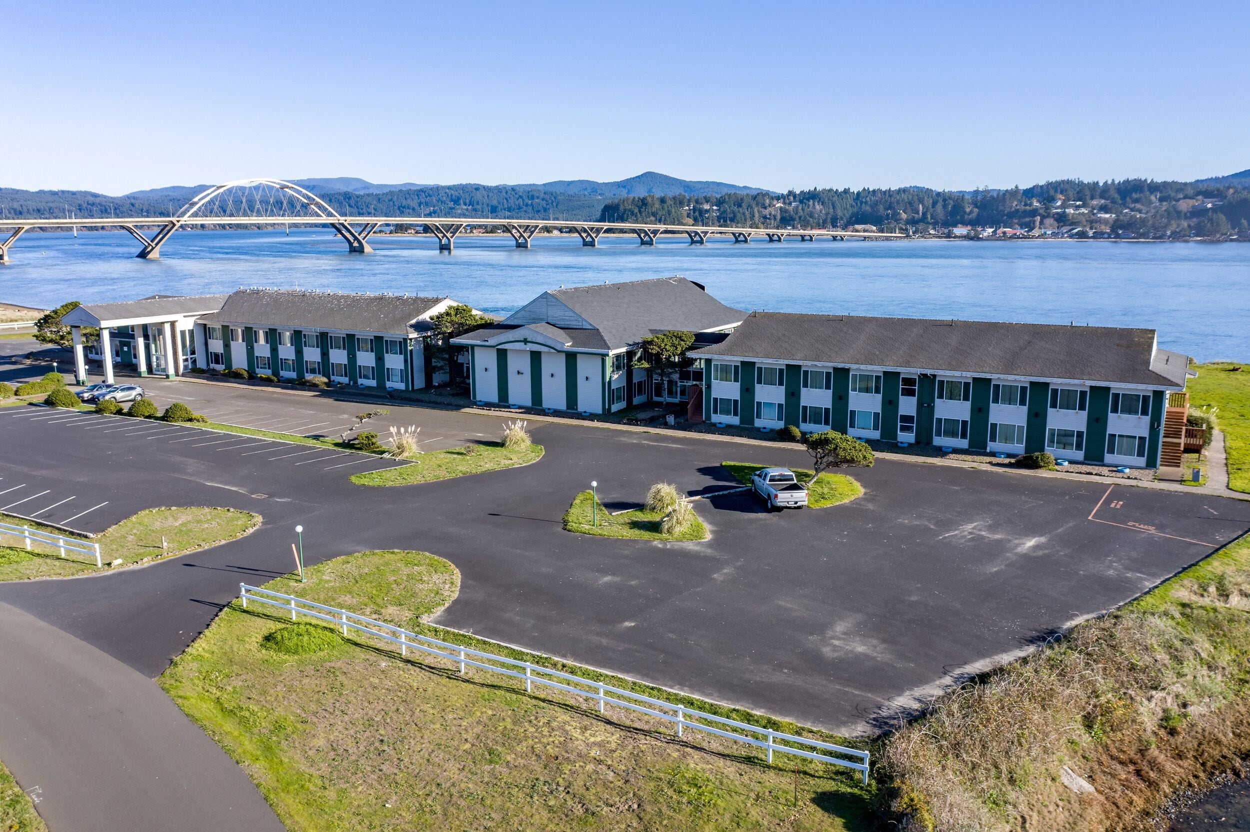A motel with a parking lot, a bridge in the background, and a view of the water.
