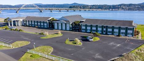 A motel with a parking lot, a bridge in the background, and a view of the water.