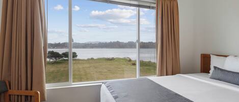 Un dormitorio con un ventanal grande, una cama, una silla y vistas a un cuerpo de agua.