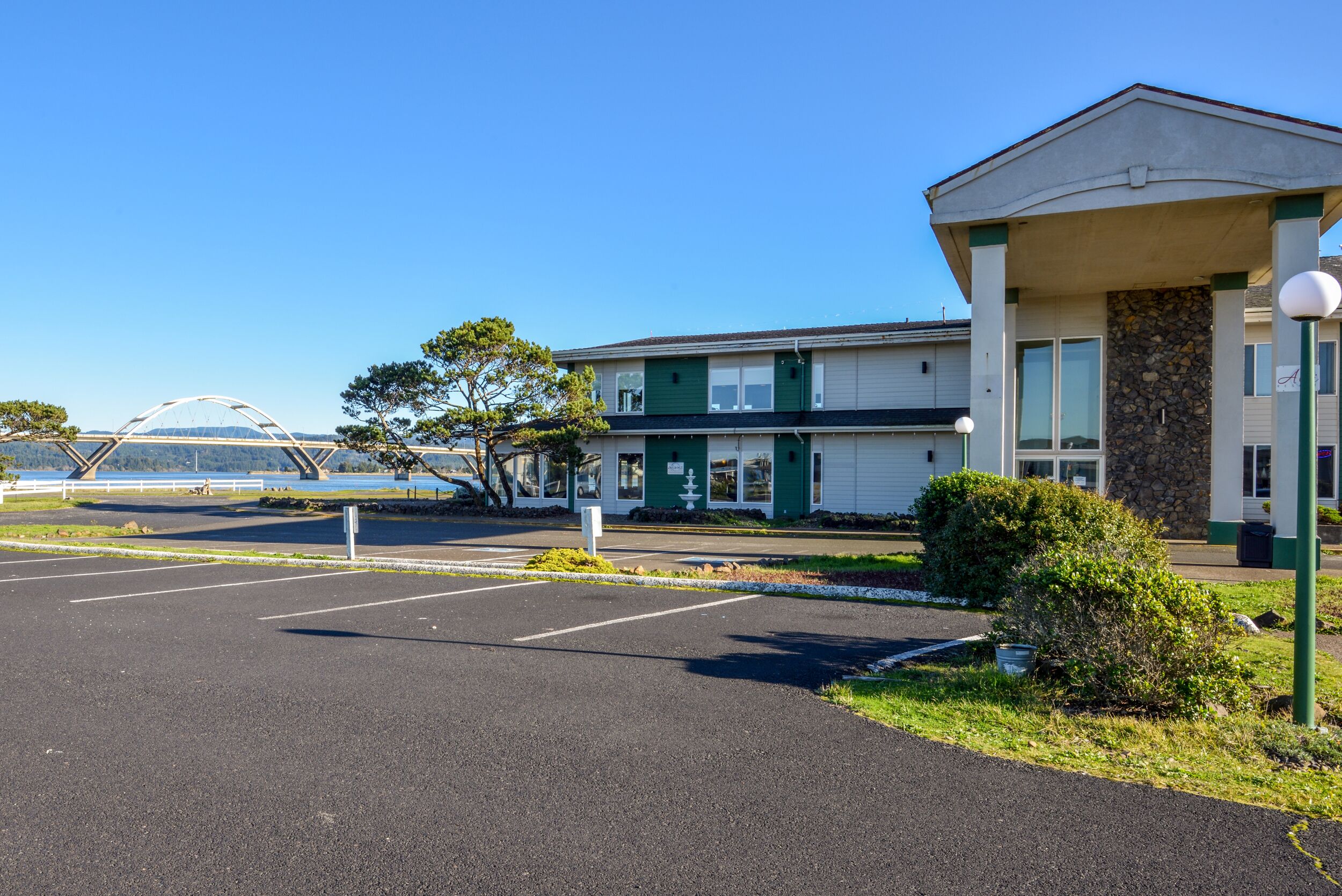 A building with a parking lot, a covered area, and a view of a bridge and water.