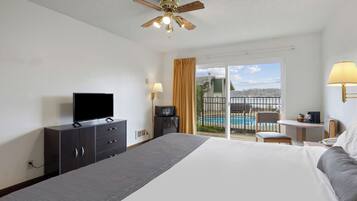 A hotel room with a bed, a television, a desk with a lamp, a chair, and a view of a swimming pool.