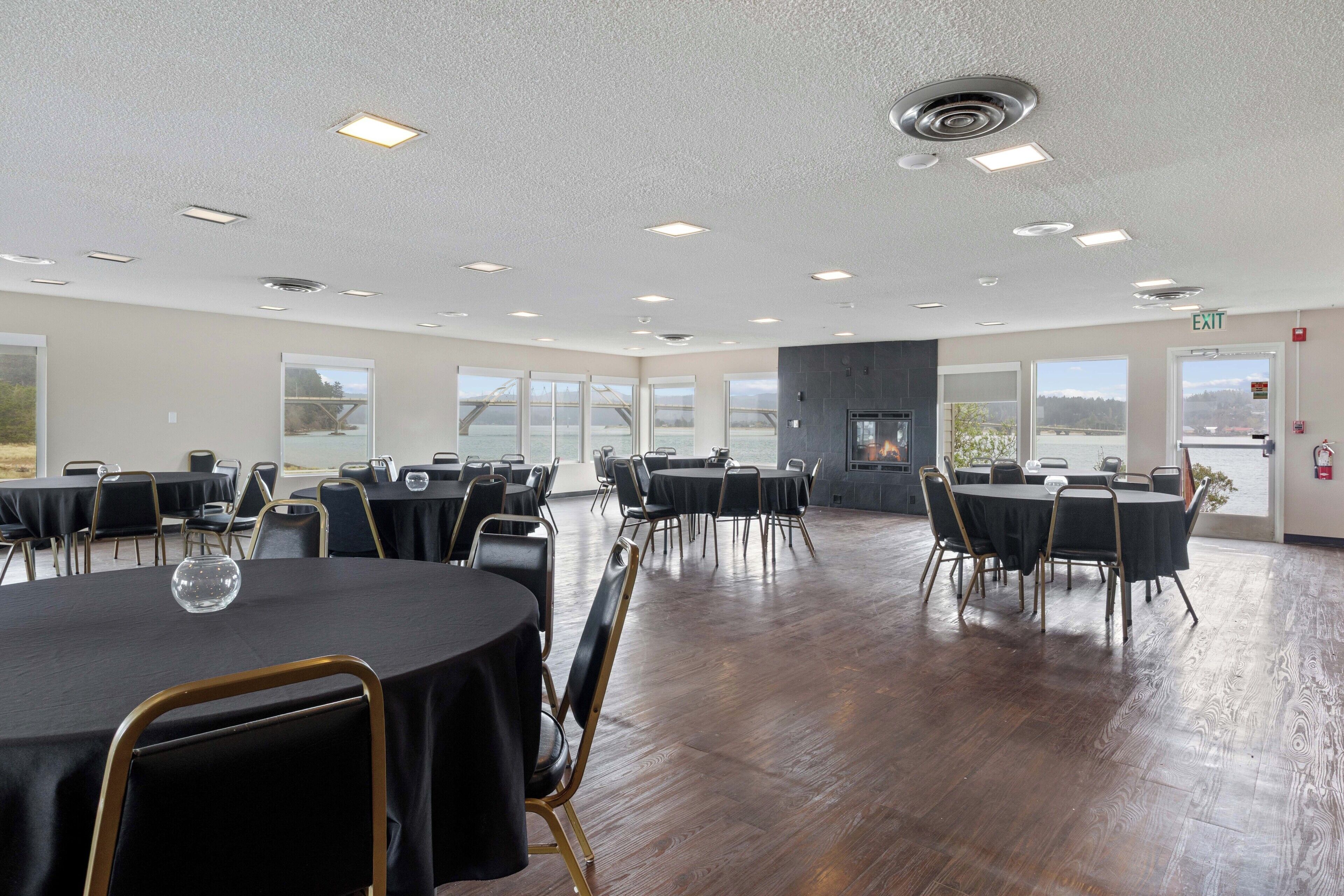 A spacious conference room with multiple tables and chairs, large windows with a view, and a fire extinguisher on the wall.