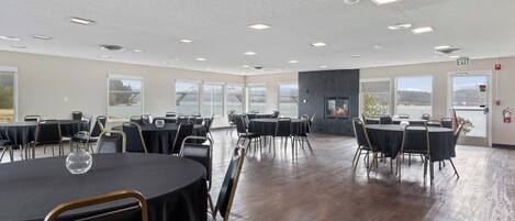 A spacious conference room with multiple tables and chairs, large windows with a view, and a fire extinguisher on the wall.