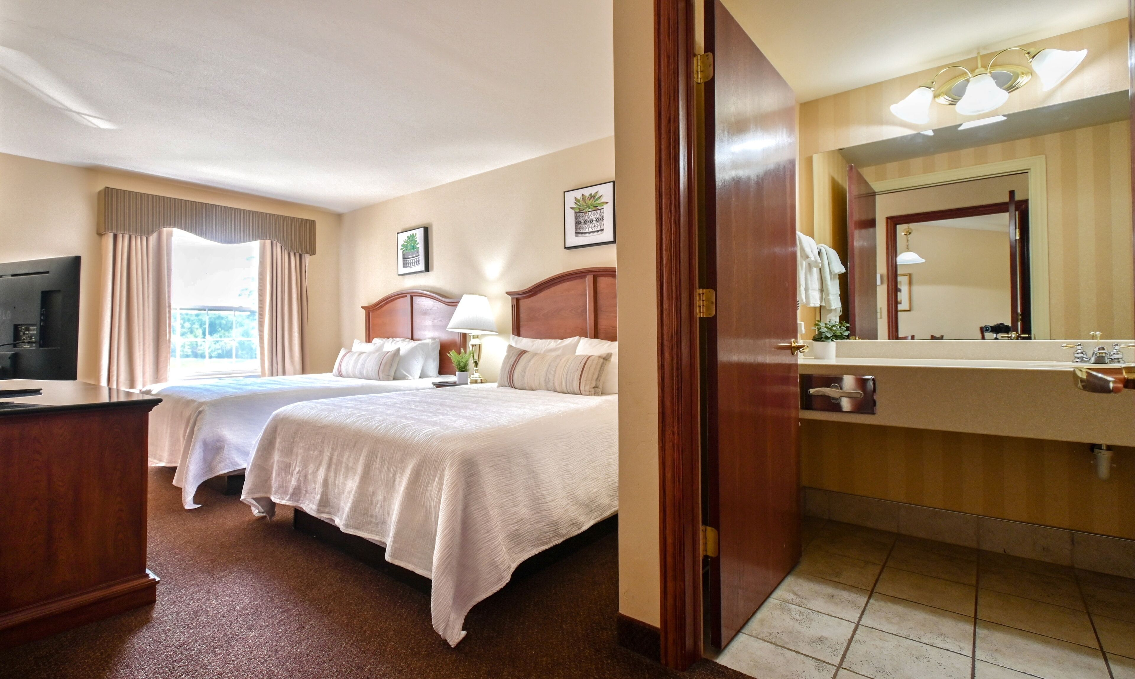 Een hotelkamer met twee bedden, een televisie, een bureau, een badkamer met spiegel en een raam met gordijnen.