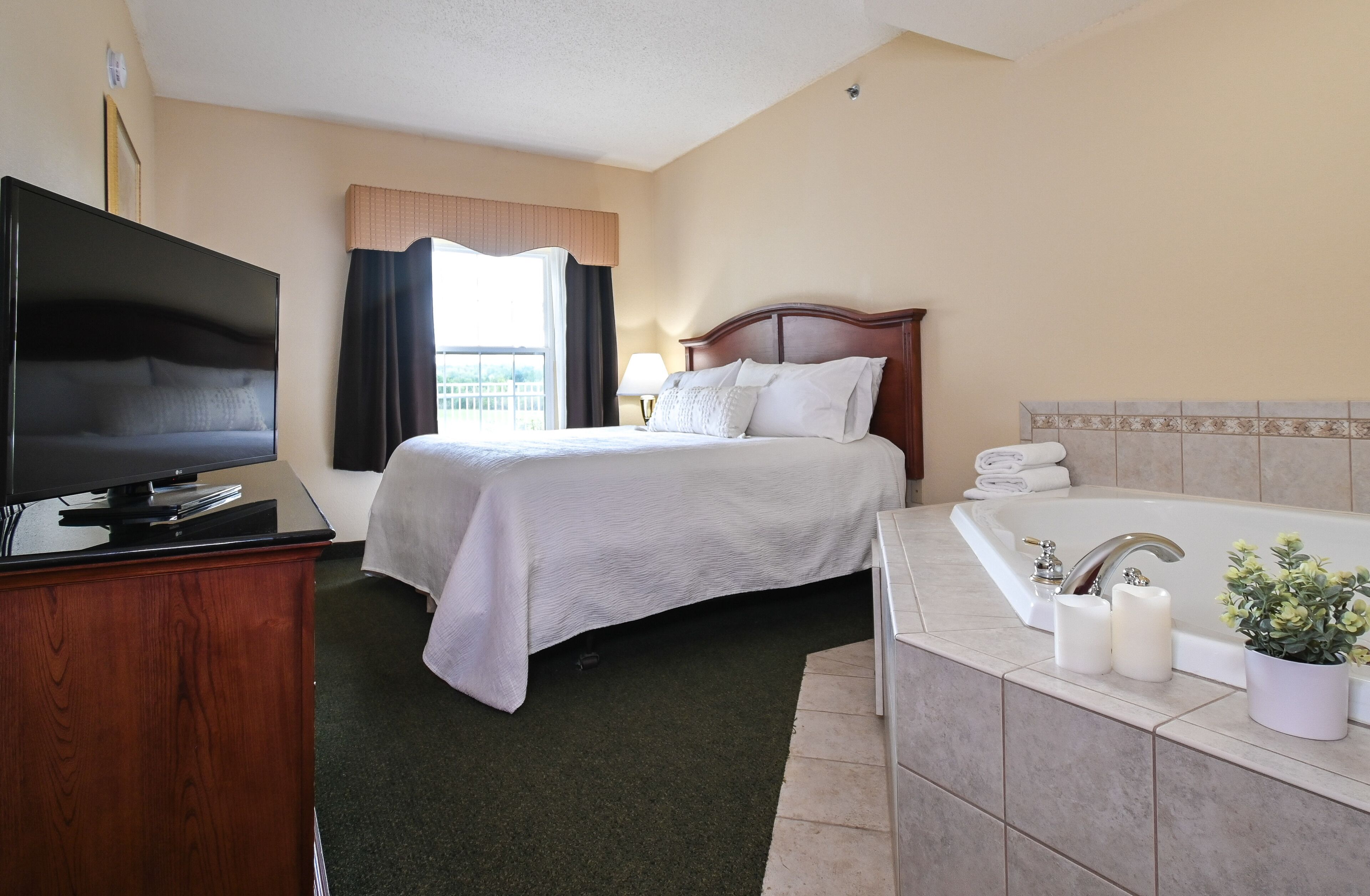 A hotel room with a bed, a television, a bathroom with a bathtub, and a window with curtains.
