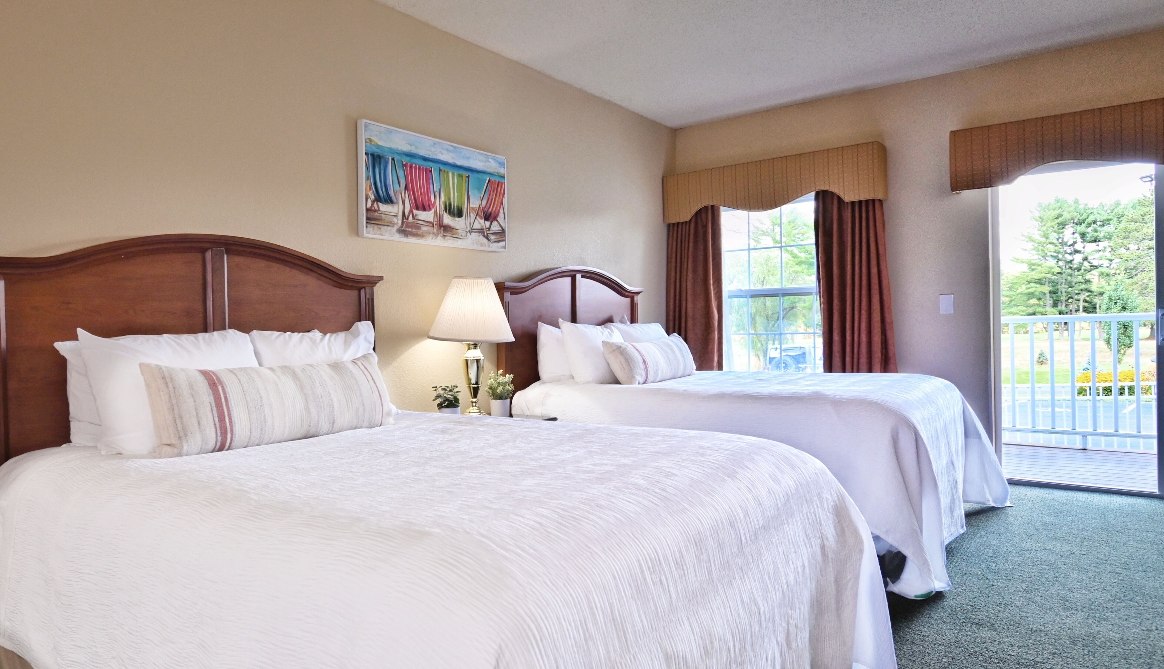 A hotel room with two beds, a painting on the wall, a window with curtains, and a view of the outdoors.