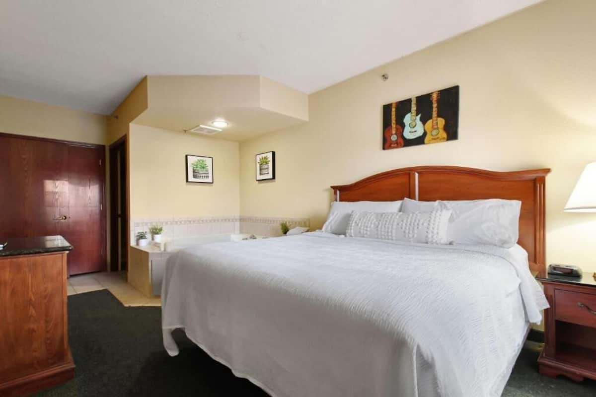 Une chambre d’hôtel avec un grand lit, une armoire en bois, une petite table de chevet, une commode et un tableau représentant une guitare accroché au mur.