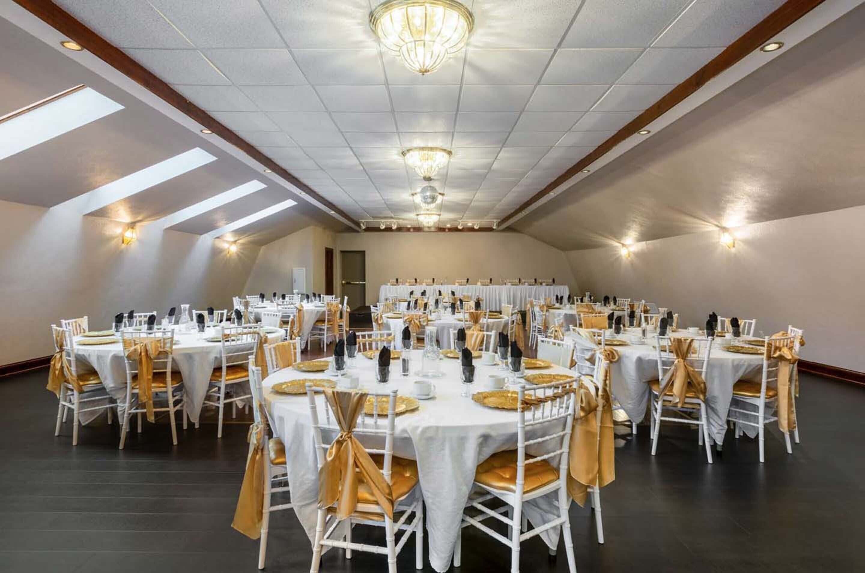 A large banquet hall with round tables, white chairs, and gold sashes.
