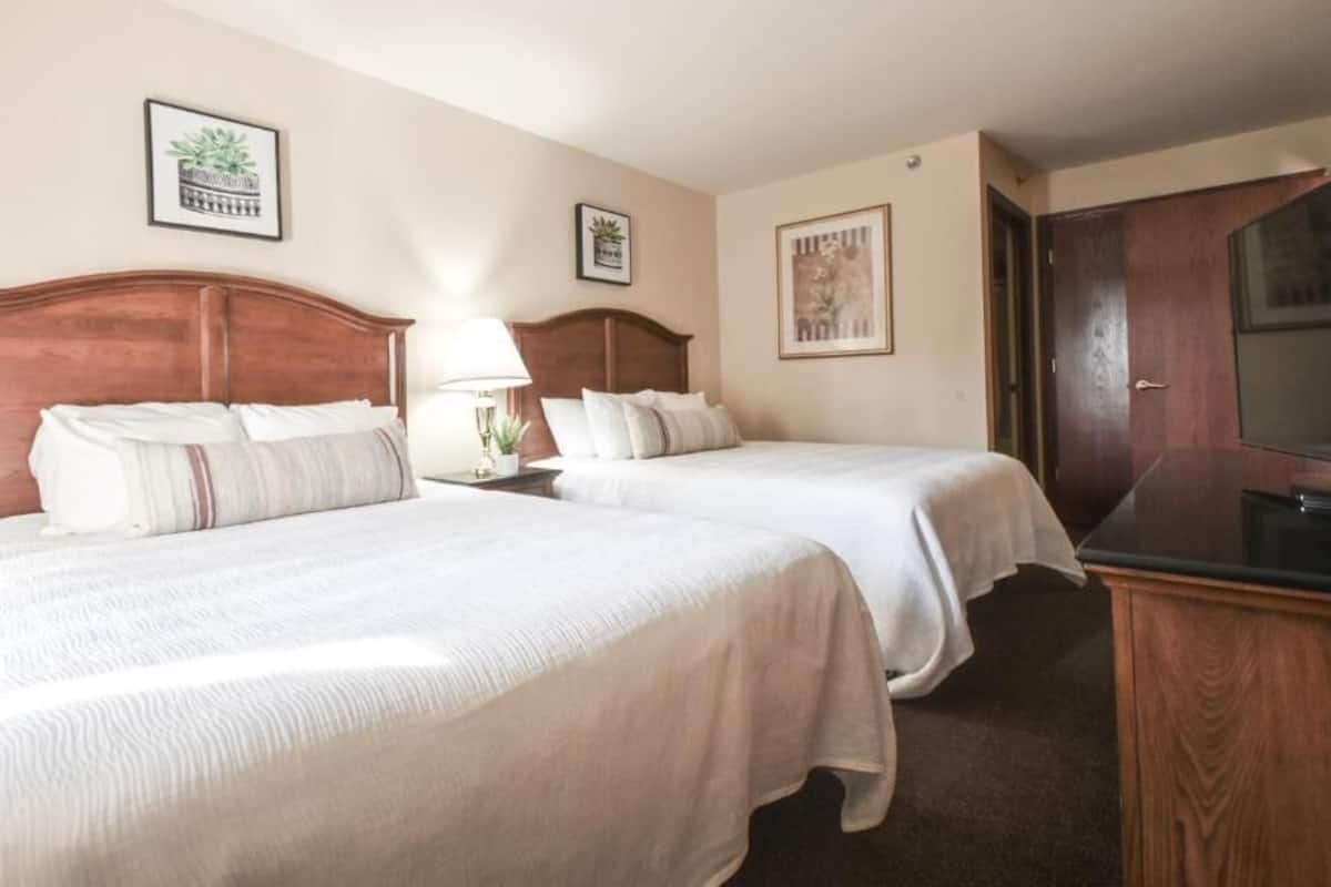 Une chambre d’hôtel avec deux lits, une télévision et un bureau avec une lampe.