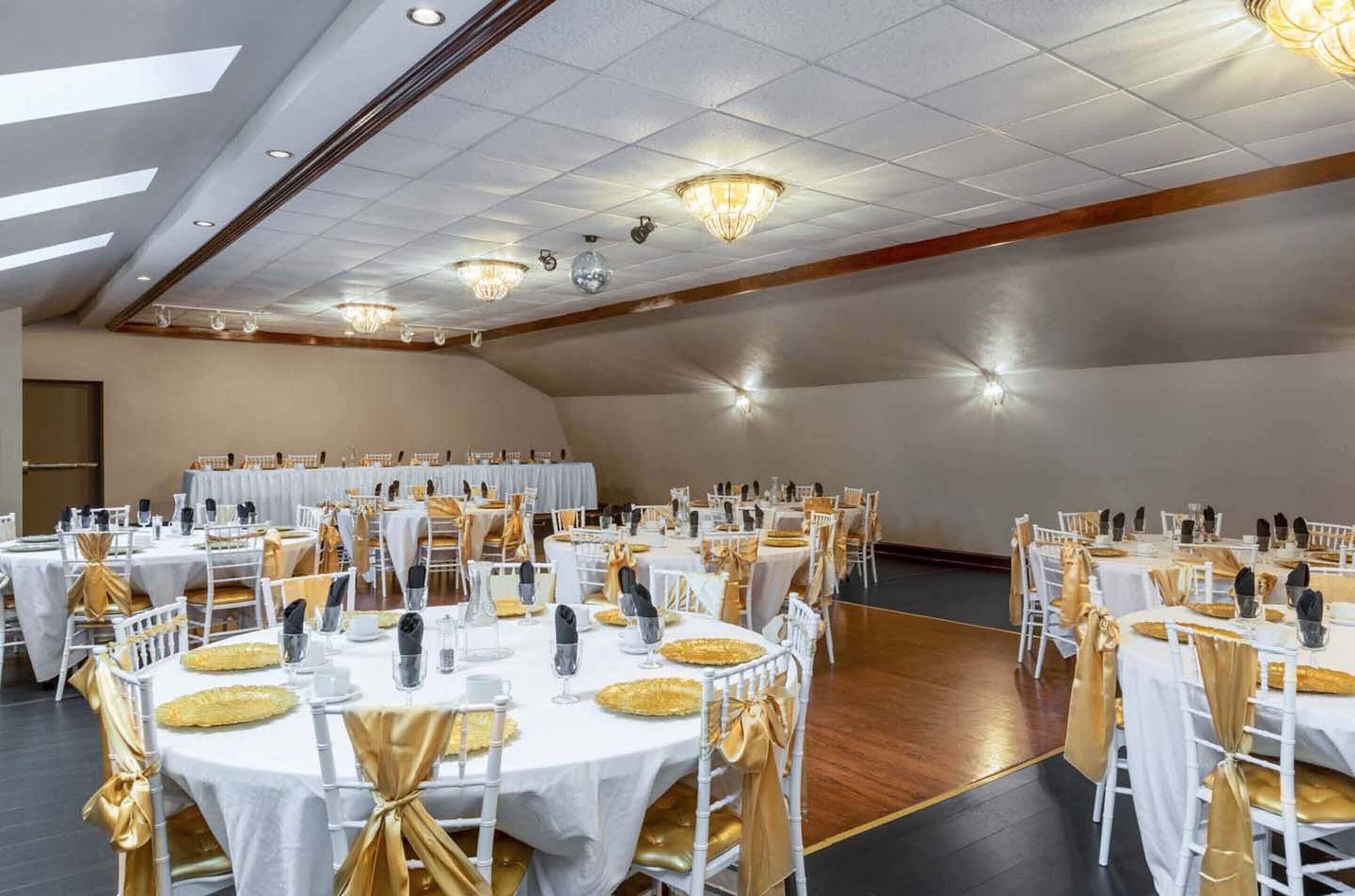 A banquet hall with round tables, white tablecloths, and gold sashes.